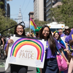 Two girls holding up a poster with a rainbow that reads "SF State PRIDE"